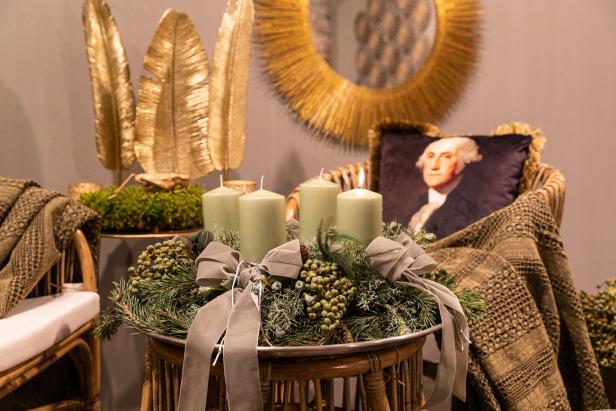 Ein Adventskranz mit vier Kerzen und Schleifen auf einem Tisch, im Hintergrund ein Kissen mit George Washington.