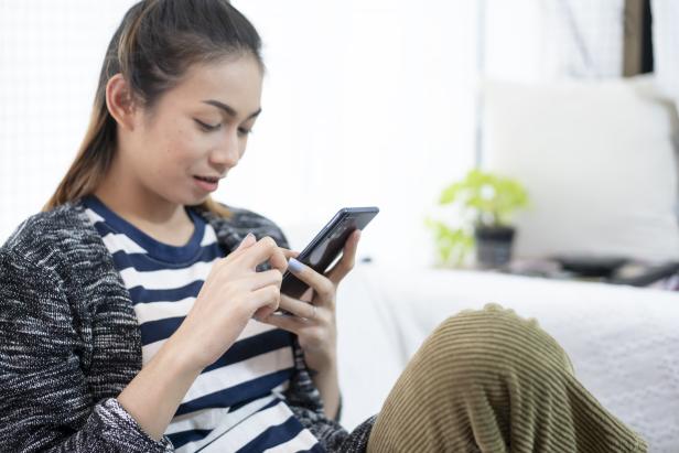 Eine Frau sitzt und tippt auf ihrem Smartphone.