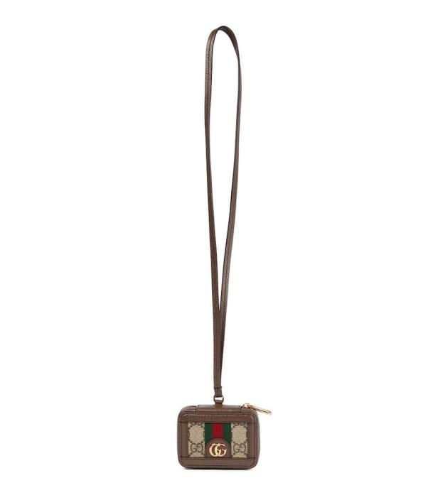 Eine kleine Gucci-Tasche mit braunem Riemen hängt vor einem weißen Hintergrund.
