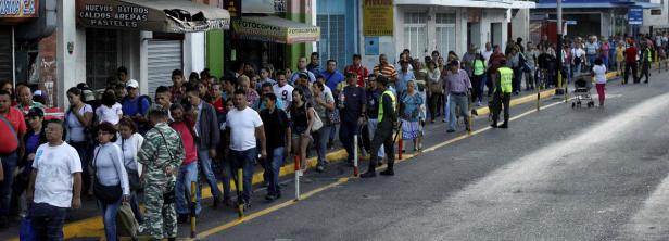 Eine lange Schlange von Menschen steht auf einer Straße vor Geschäften an.