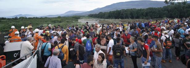 Eine große Menschenmenge überquert eine Brücke in einer ländlichen Gegend.