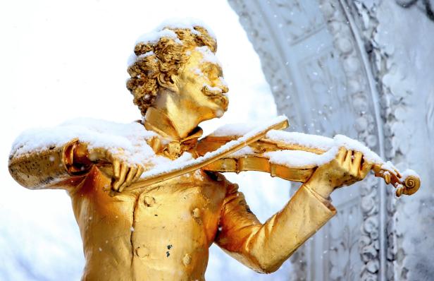 Eine goldene Statue von Johann Strauss spielt im Schnee Geige.