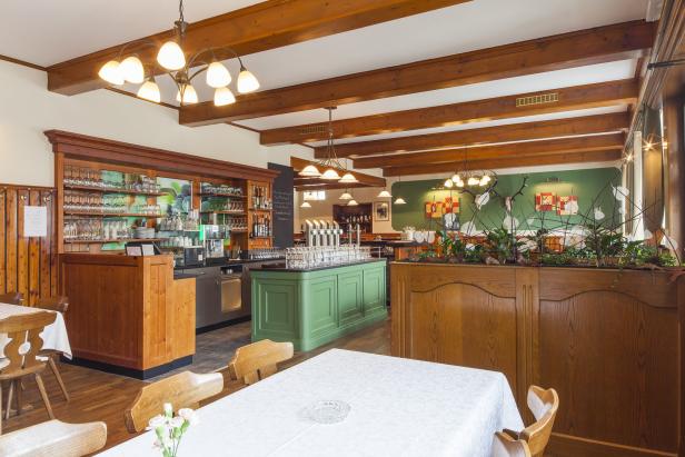 Innenansicht eines traditionellen Restaurants mit Holzbalken und grüner Bar.