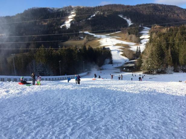 Auf einer schneebedeckten Fläche sind Menschen beim Rodeln und Spielen zu sehen.