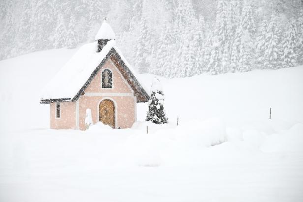 Eine kleine, schneebedeckte Kapelle steht inmitten eines verschneiten Waldes.