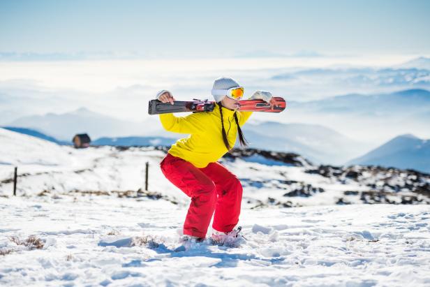 Eine Skifahrerin mit Skiern auf den Schultern steht im Schnee.