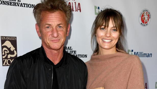 Sean Penn und eine Frau posieren lächelnd vor einer Sponsorenwand.