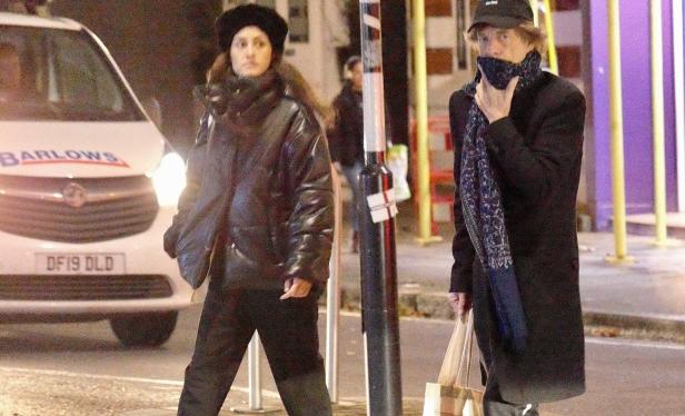 Mick Jagger und eine Frau gehen nachts auf der Straße.