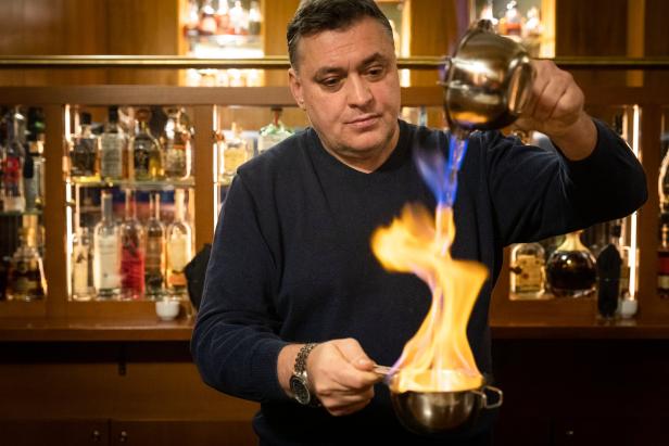 Ein Barkeeper flambiert einen Drink vor einer Bar mit Spirituosenflaschen.
