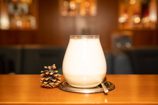 Ein cremiger Cocktail steht neben einem Tannenzapfen auf einem Tisch.