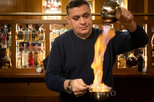 Ein Barkeeper flambiert ein Getränk vor einer Bar mit Spirituosenflaschen.
