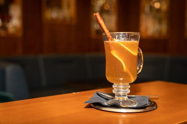 Ein Glas Apfelwein mit Zimtstange und Orangenschale auf einem Tisch.