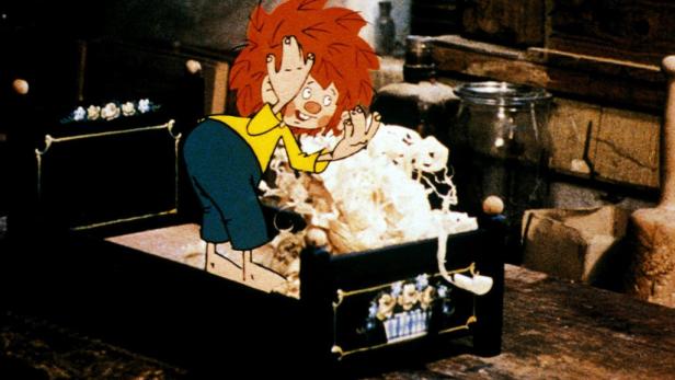 Pumuckl steht an einem kleinen Bett und schüttelt das Kissen aus.