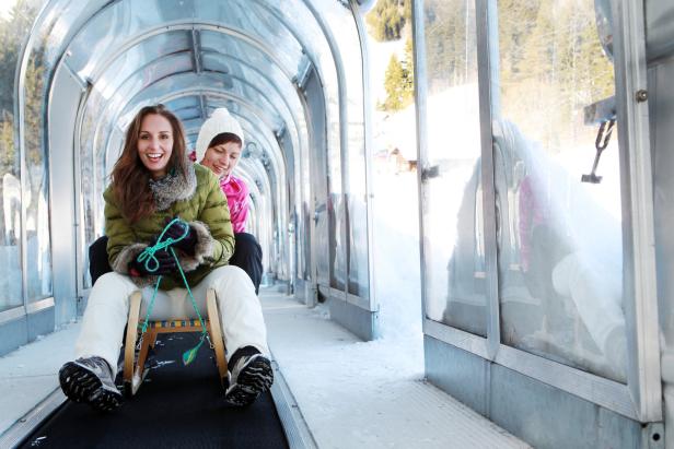 Zwei Frauen rodeln in einem Tunnel auf einer Rodelbahn.