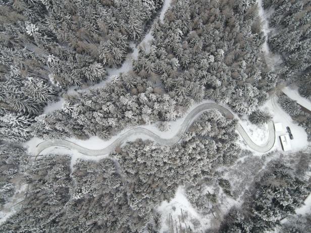 Luftaufnahme einer kurvenreichen, schneebedeckten Straße durch einen verschneiten Wald.