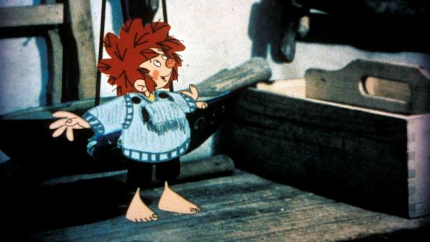 Ein barfüßiger Pumuckl steht in einer Werkstatt.