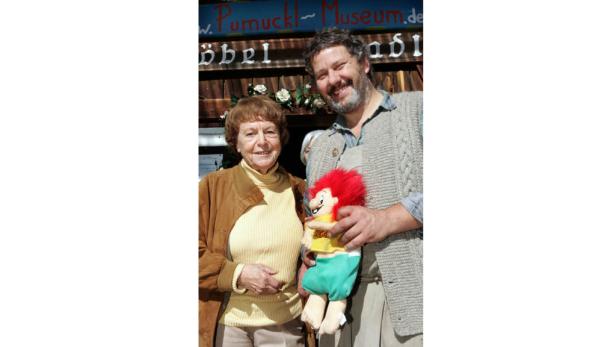 Eine Frau und ein Mann halten eine Pumuckl-Puppe vor dem Pumuckl-Museum.