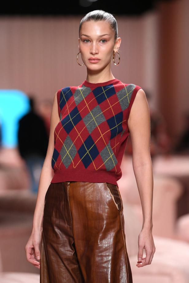 Bella Hadid trägt einen Argyle-Pullunder und eine glänzende Hose auf dem Laufsteg.
