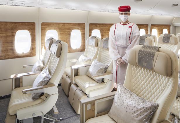 Eine Stewardess mit Maske steht in einer leeren Emirates-Flugzeugkabine.