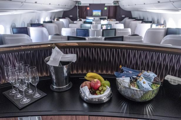 Im Vordergrund stehen Getränke und Snacks in einem luxuriösen Flugzeuginnenraum.
