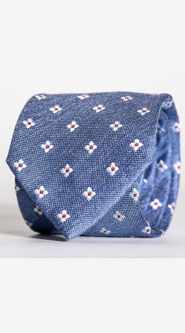 Eine zusammengerollte, blaue Krawatte mit einem Muster aus kleinen, weißen Blumen mit roten Punkten.
