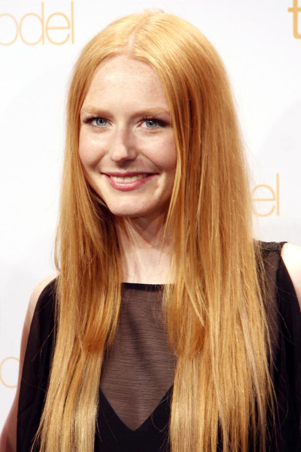 Eine Frau mit langen roten Haaren und einem schwarzen Oberteil lächelt.