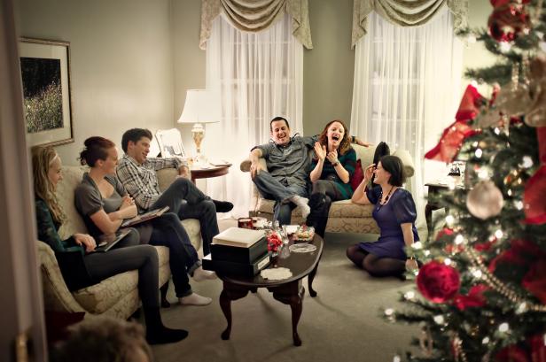 Eine Gruppe von Freunden sitzt im Wohnzimmer um einen Weihnachtsbaum herum und unterhält sich.