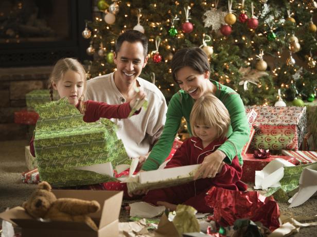 Eine Familie sitzt vor einem Weihnachtsbaum und packt Geschenke aus.