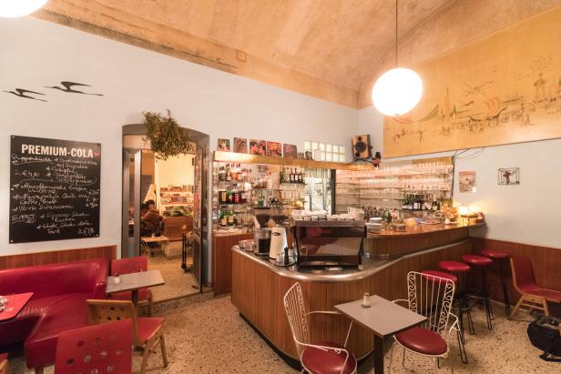 Innenansicht eines Cafés mit Bar, Tischen und Stühlen.