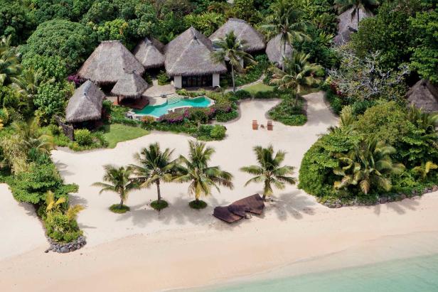 Luftaufnahme von strohgedeckten Hütten mit Pool an einem tropischen Strand.