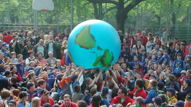 Eine große Gruppe von Menschen hält einen Globus in die Höhe.