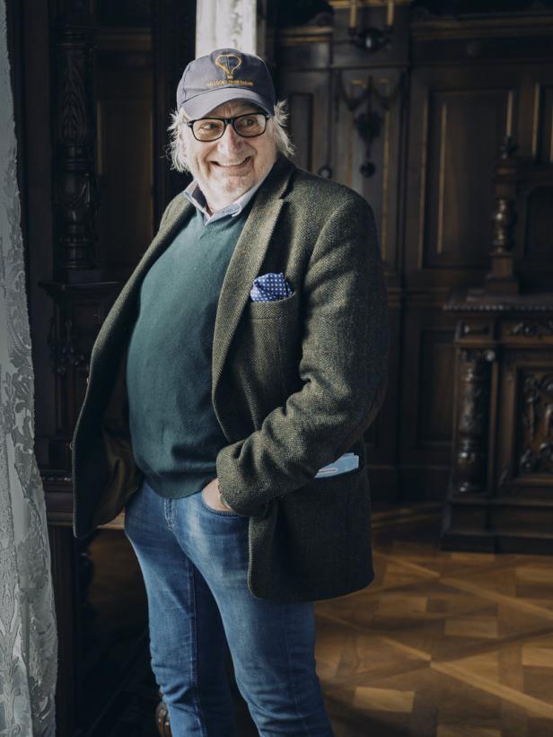 Ein lächelnder Mann mit Brille und Kappe posiert in einem eleganten Raum.