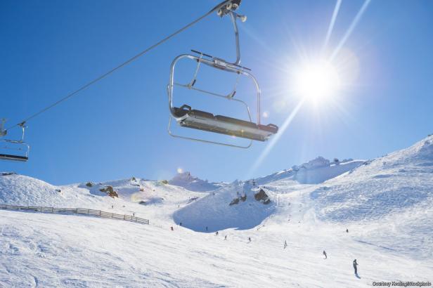 Ein Sessellift fährt über eine schneebedeckte Skipiste an einem sonnigen Tag.