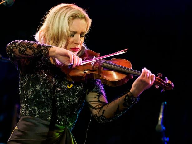 Eine Frau mit blonden Haaren spielt auf einer Bühne Geige.