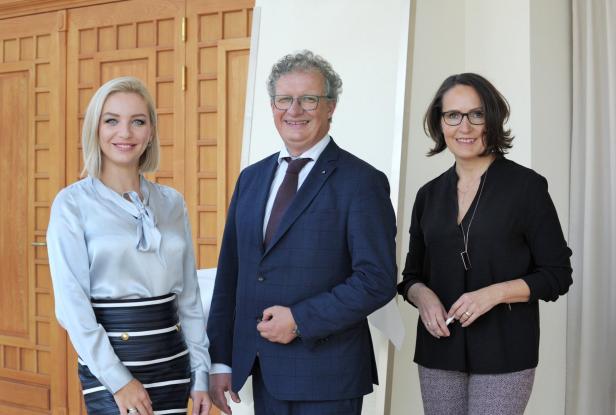 Drei Personen posieren vor einer Holztür und einer weißen Wand.