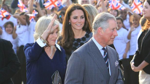 König Charles, Königin Camilla und Prinzessin Kate inmitten einer Menschenmenge mit Union-Jack-Flaggen.