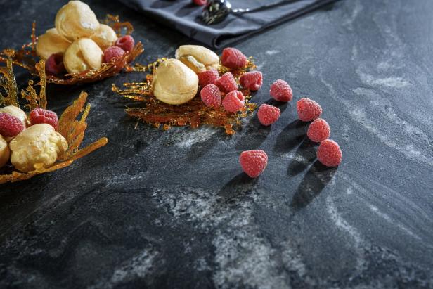 Windbeutel und Himbeeren auf einer dunklen Oberfläche mit Karamellgarnitur.