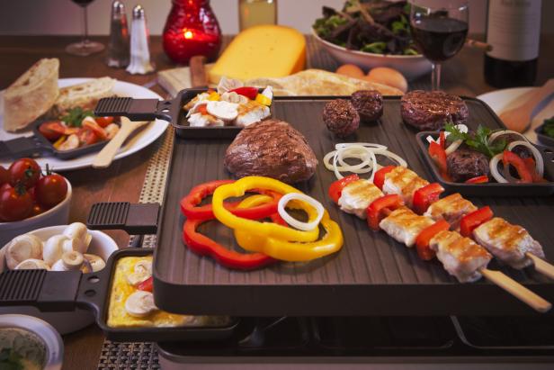 Ein Raclette-Grill mit Fleisch, Gemüse und Käse auf einem Tisch angerichtet.