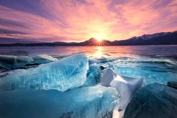 Eisblöcke liegen auf einem gefrorenen See bei Sonnenaufgang.