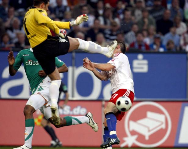 Ein Fußballspiel, bei dem ein Torwart einen Spieler mit dem Fuß abwehrt.
