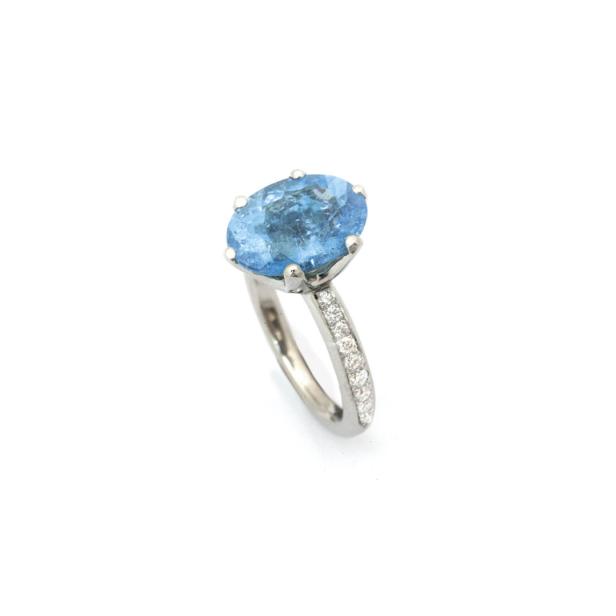 Ein Ring mit einem großen, ovalen, hellblauen Stein und kleinen Diamanten auf der Ringschiene.
