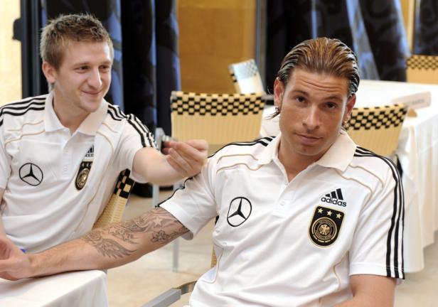 Zwei deutsche Fußballspieler in ihren Trikots sitzen an einem Tisch.