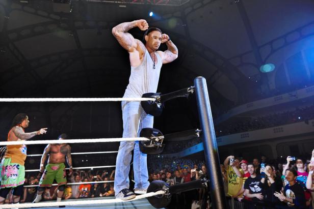 Ein tätowierter Wrestler steht im Ring und posiert vor einem Publikum.