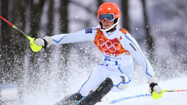 Eine Skirennläuferin mit orangerfarbenem Helm fährt einen Hang hinunter.