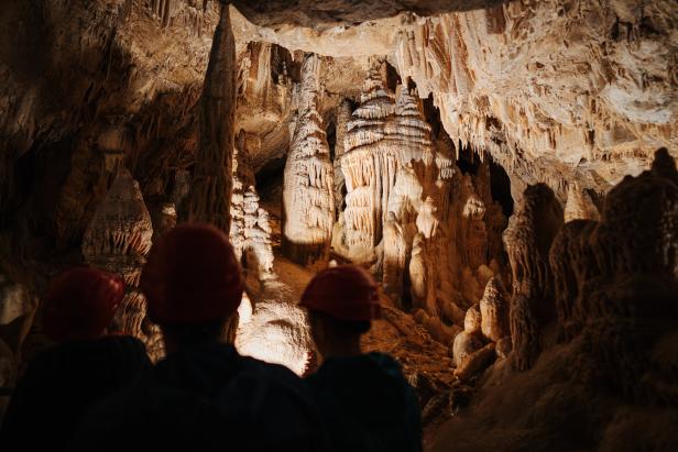 Besucher mit Helmen betrachten Stalaktiten und Stalagmiten in einer Höhle.