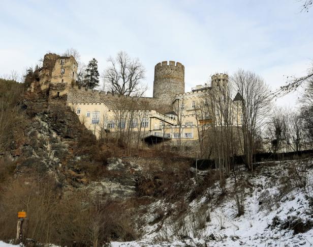 Eine Burg mit einem runden Turm steht auf einem Hügel mit etwas Schnee.