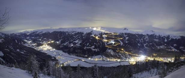 Nachts beleuchtete Skipiste schlängelt sich einen schneebedeckten Berg hinauf.