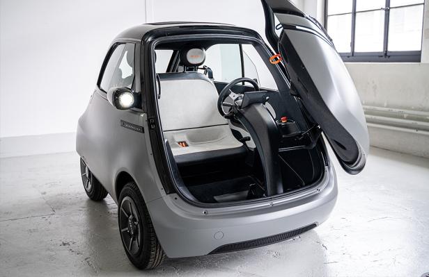 Ein graues Microlino-Auto mit geöffneter Fronttür steht in einem Studio.