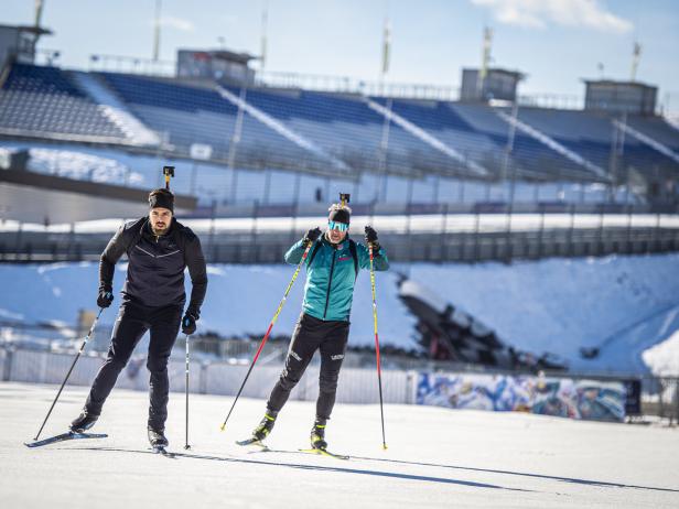 Zwei Biathleten trainieren auf Skiern vor einer Zuschauertribüne.