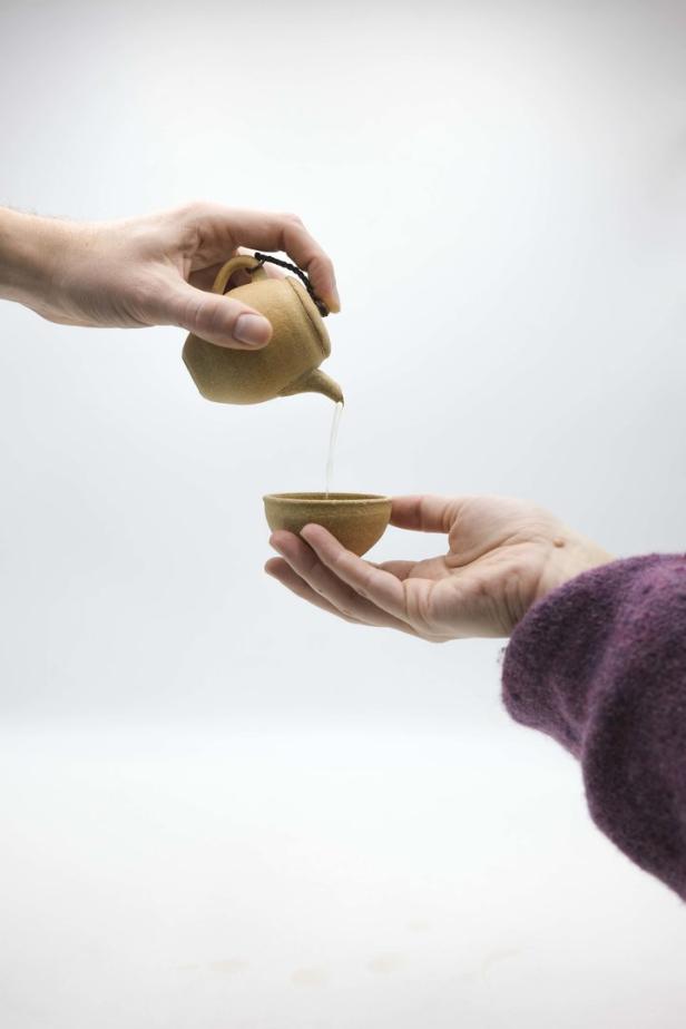 Eine Hand gießt Tee aus einer kleinen Kanne in eine Tasse, die von einer anderen Hand gehalten wird.